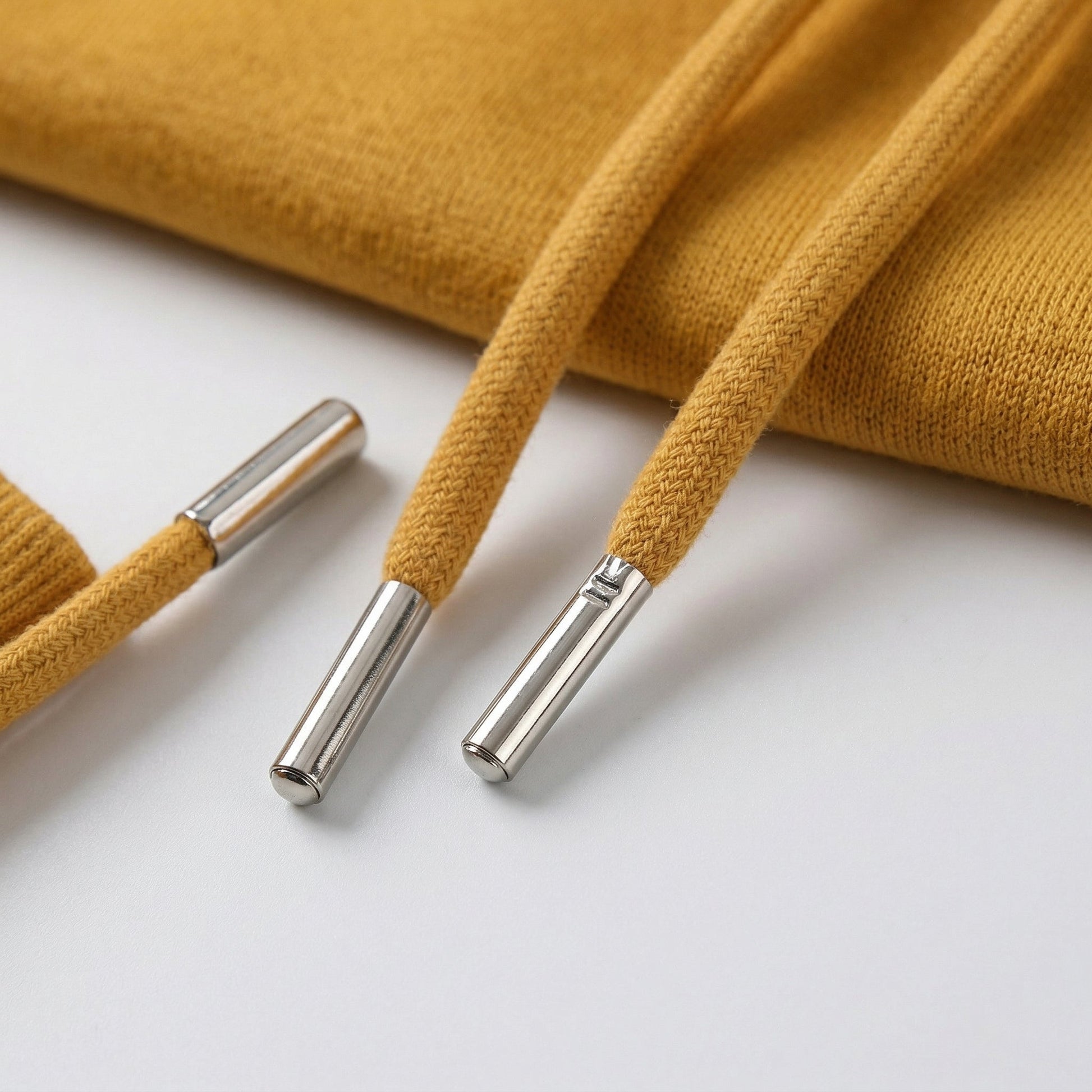 Senfgelbe Kapuzenkordeln mit silbernen Metallenden an Strickstoff