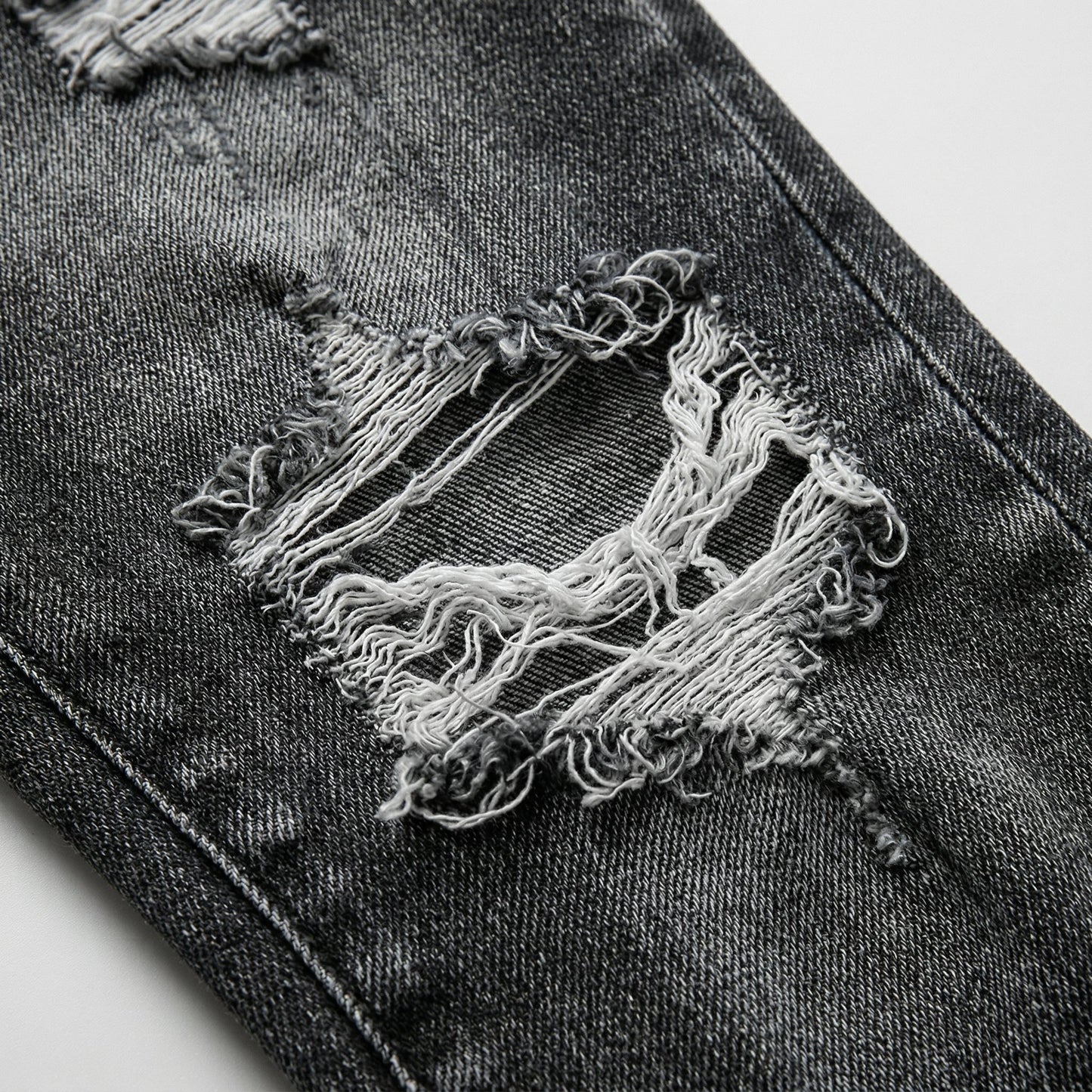 Dunkelgraue Damenjeans mit großen ausgefransten Löchern und Tassel-Details nahaufnahme