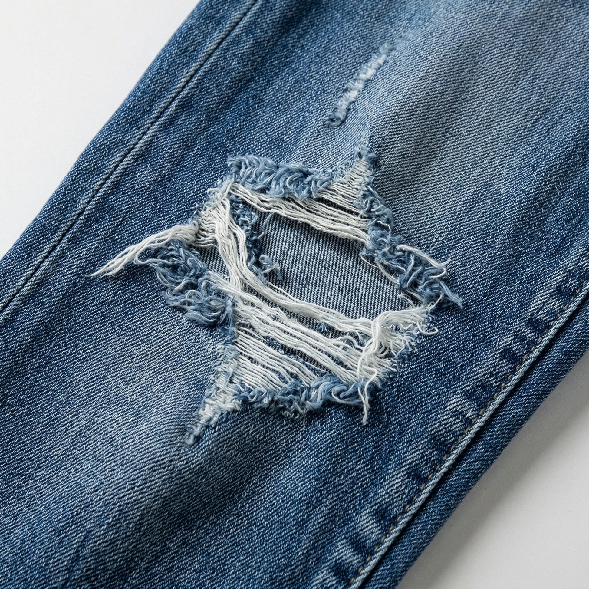 Close-up auf mittelblaue Damenjeans mit großem ausgefranstem Destroyed-Loch und weißen Fäden