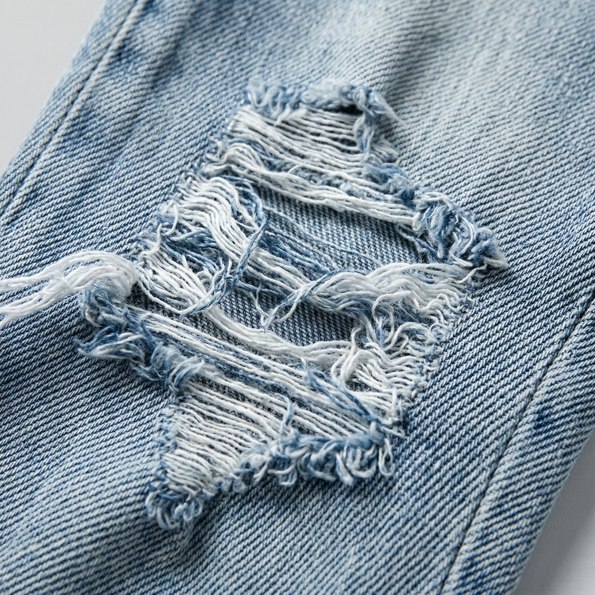 Hellblaue Jeans mit ausgefransten, modischen Rissen und sichtbarer Denim-Struktur Nahaufnahme