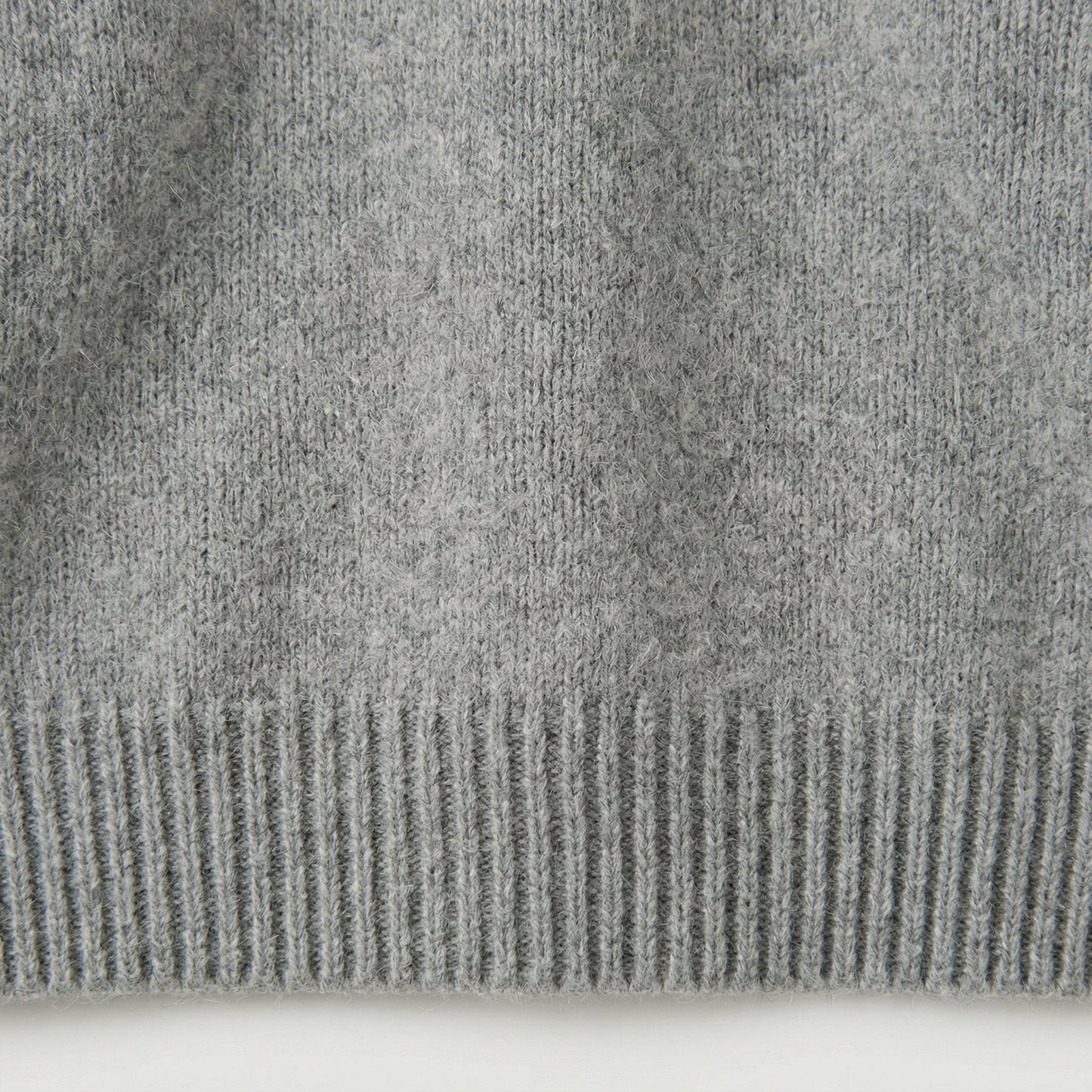 Nahaufnahme hellgrauer Strickpullover mit geripptem Saum und weicher, flauschiger Oberfläche