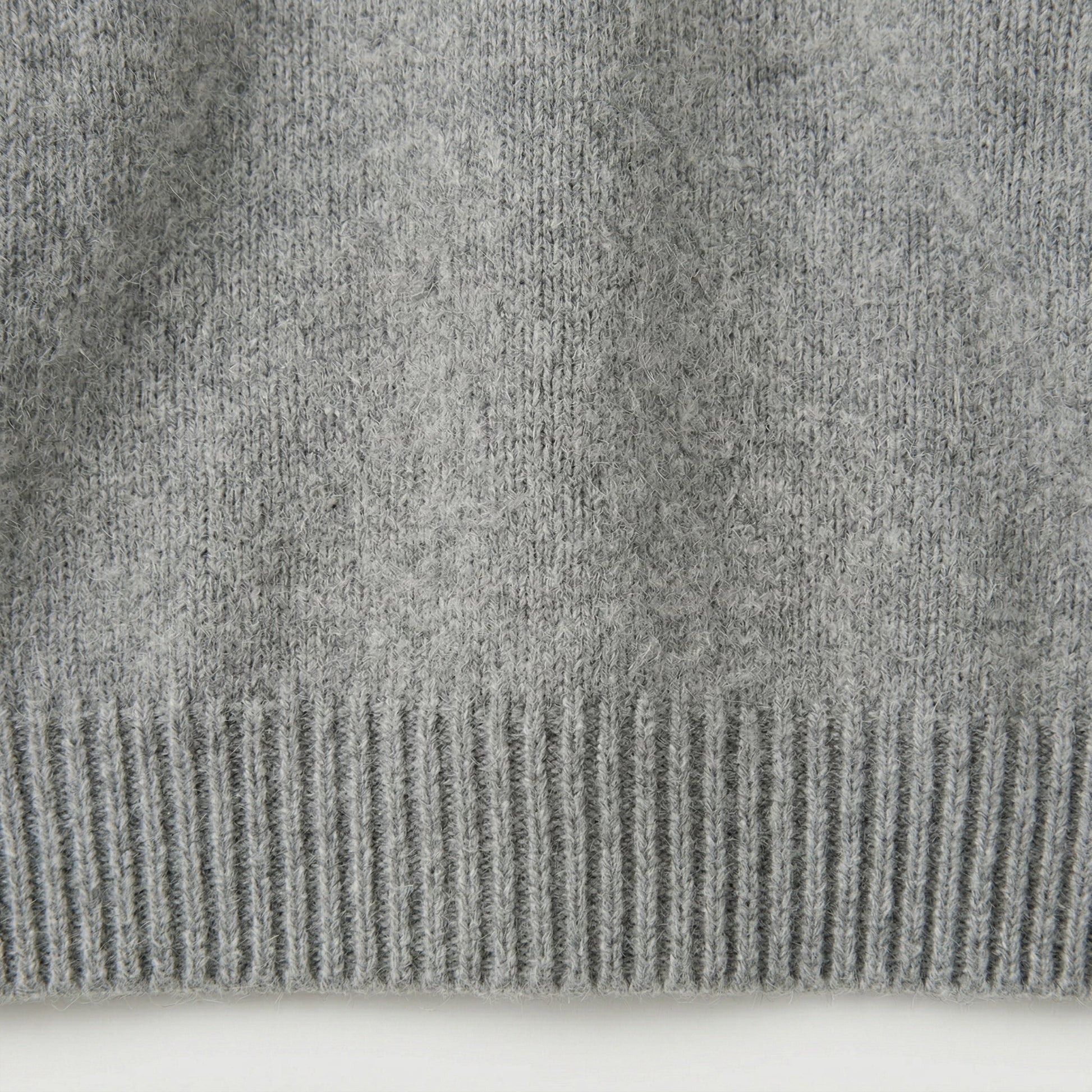 Nahaufnahme hellgrauer Strickpullover mit geripptem Saum und weicher, flauschiger Oberfläche